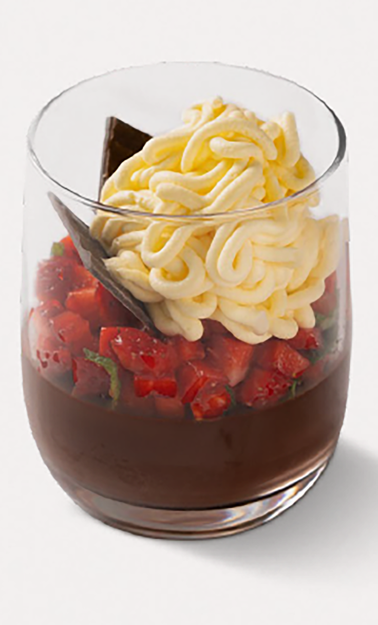 Chocolate mousse in a glass topped with diced strawberries, whipped cream swirls, and a dark chocolate shard.